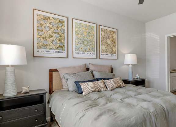 A bedroom with a bed, two lamps, and three framed pictures on the wall.