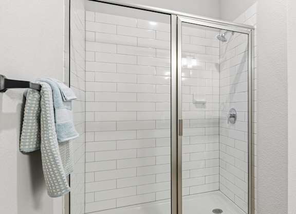 A white tiled shower with a glass door and a towel hanging on the wall.