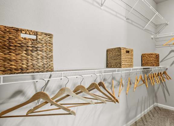A room with clothes hanging on hangers and baskets on the shelf.