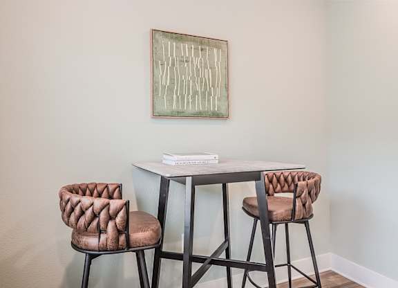A painting hangs on a wall above a table with two chairs.