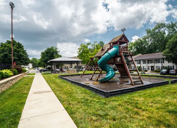 Apartments For Rent In Louisville, KY - Enclave At Breckenridge - Playground Surrounded By Grass with Concrete Walking Path Near Parking Lot And BBQ Area.