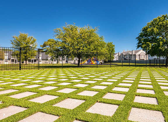 A park with a black fence and a green lawn with white rectangular stones.