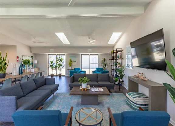 A living room with a grey sofa, blue chairs, and a television on the wall.