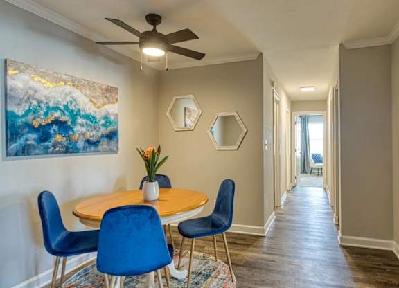 A dining room with a table and chairs and a painting on the wall.