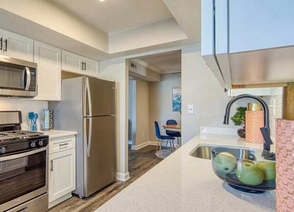 A kitchen with a stove, oven, refrigerator, and a bowl of fruit on the counter.