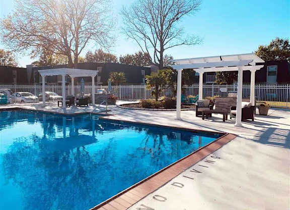 A pool with a white pergola and a bench.