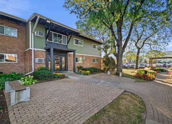 a brick and green building with a walkway and trees