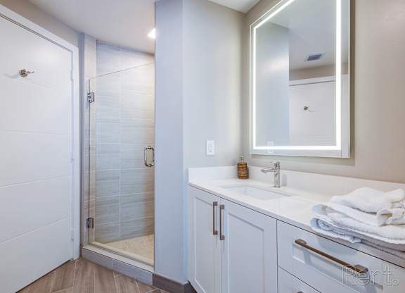 A white bathroom with a sink, mirror, and shower.