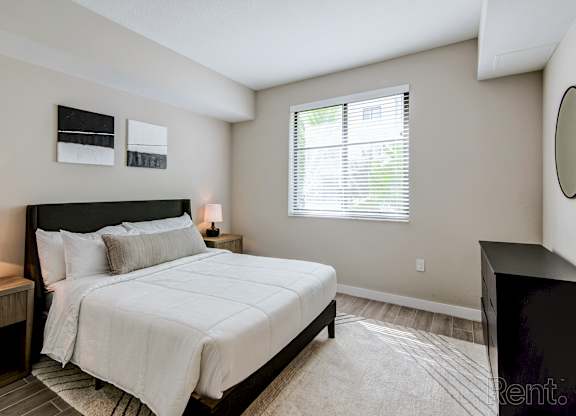A bedroom with a large bed and a window with blinds.
