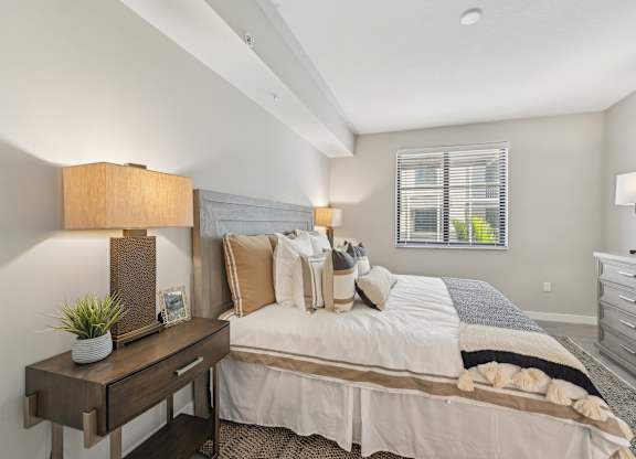 A well-lit bedroom with a large bed and a nightstand with a lamp.