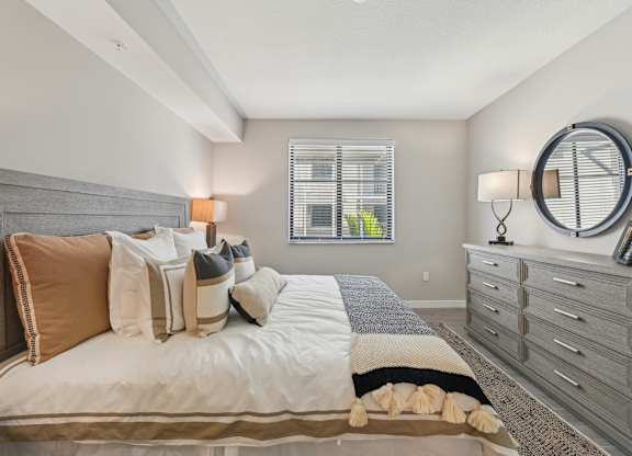 A bedroom with a bed, a dresser, and a window with blinds.
