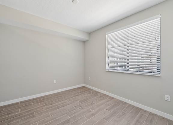 A room with a window covered by white blinds and wooden flooring.