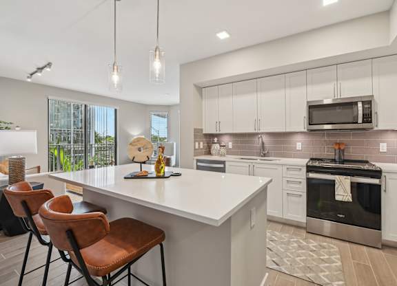 A modern kitchen with white countertops and brown leather chairs.