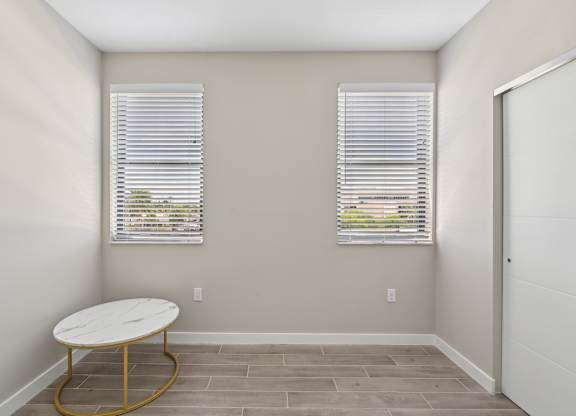 A room with a round table and two windows with blinds.