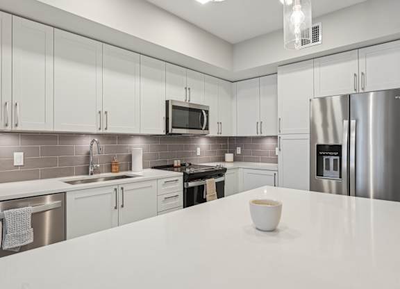 A modern kitchen with a white countertop and stainless steel appliances.