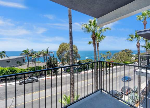 A balcony with a view of the ocean and palm trees.