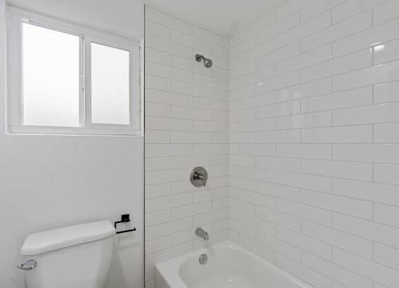 A white bathroom with a tub and toilet. at Torrance Gateway Apartments, Torrance, CA