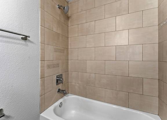 A white bathtub is in a bathroom with beige tiles.