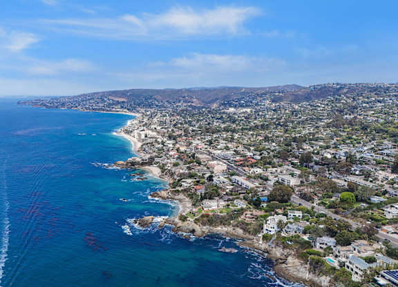 A coastal cityscape with a clear blue sky and a wake in the water from a boat.