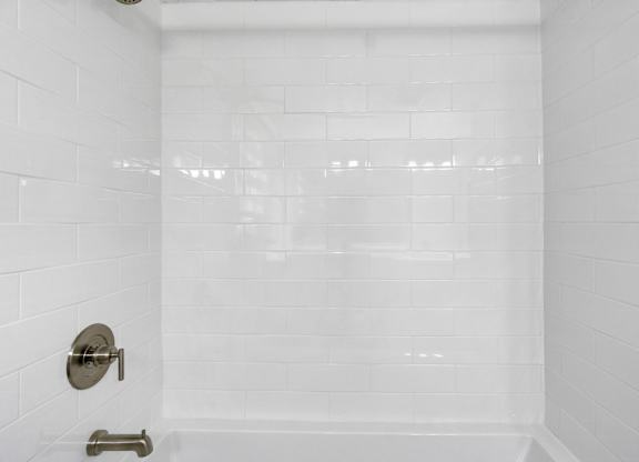 A white tiled shower with a silver faucet and a silver handle.