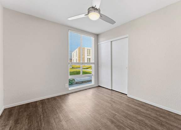 A room with a ceiling fan and a view of a building outside the window.