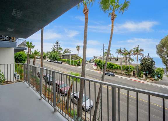A balcony overlooks a street with cars and palm trees.