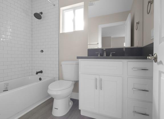 A white toilet sits in a bathroom with a white tub and a white sink.