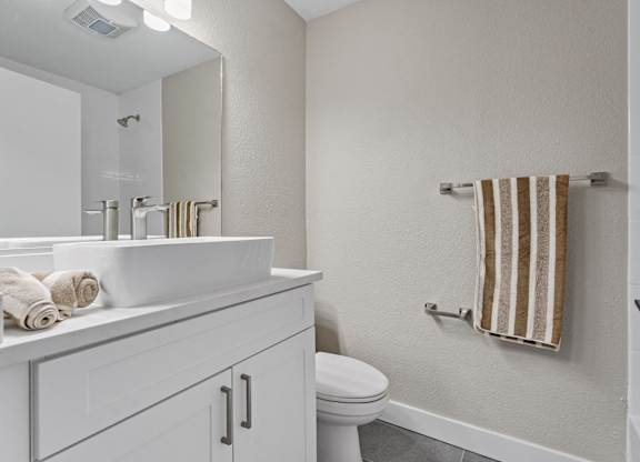 A white bathroom with a toilet, sink, and towel at Tamarack Sands Apartment Homes, California