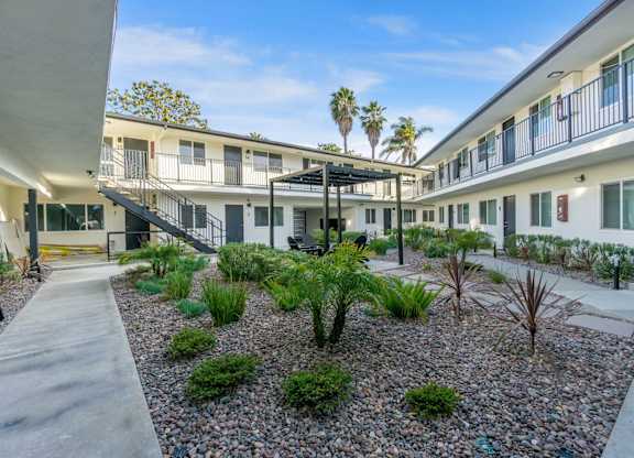 A courtyard with a variety of plants and a building in the background. at Torrance Gateway Apartments, Torrance, CA, 90501