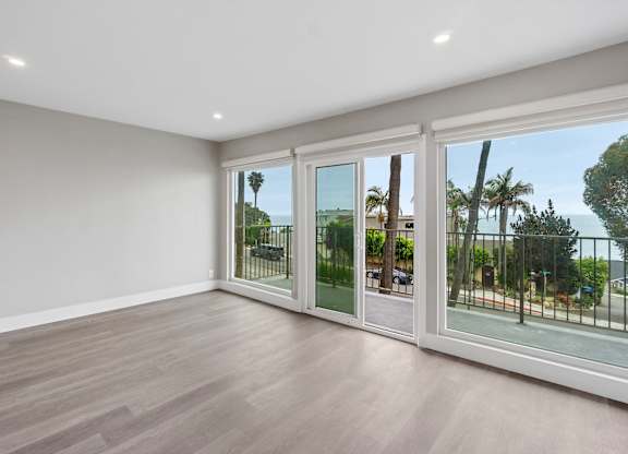 A room with a view of a street and palm trees through the glass doors.