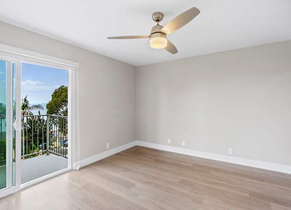 A room with a ceiling fan and sliding glass doors.
