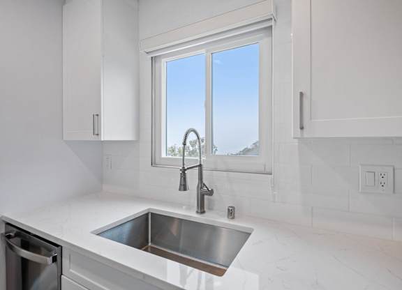 A modern kitchen with a stainless steel sink and white cabinets.