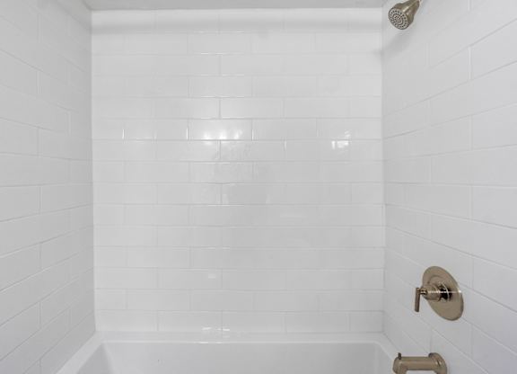 A white tiled shower with a shower head and faucet.