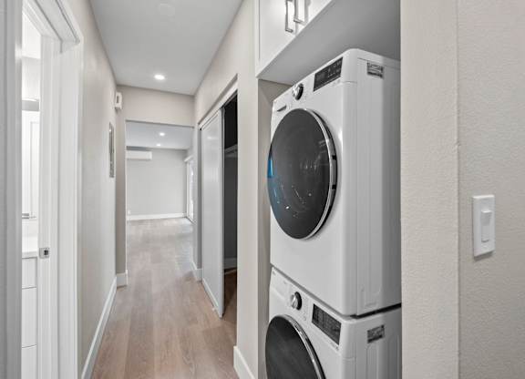 A white washing machine is stacked on top of another white washing machine in a narrow hallway.