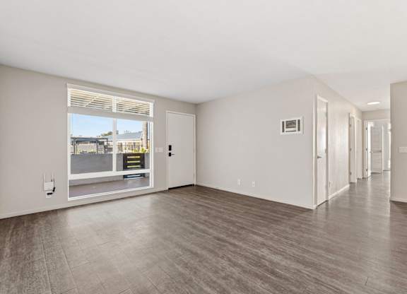 A spacious room with a large window and wooden flooring.