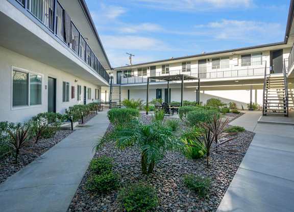 A concrete walkway leads between two buildings with a landscaped area in the middle. at Torrance Gateway Apartments, California, 90501