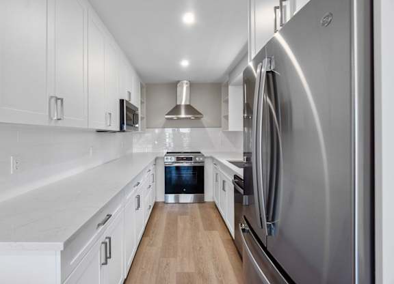 A modern kitchen with a stainless steel refrigerator and wooden flooring.