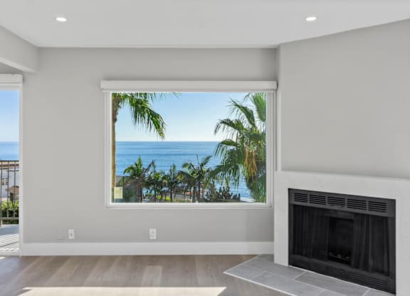 A modern living room with a fireplace and a view of the ocean through a large window.at Ocean Edge @ Laguna Beach, California