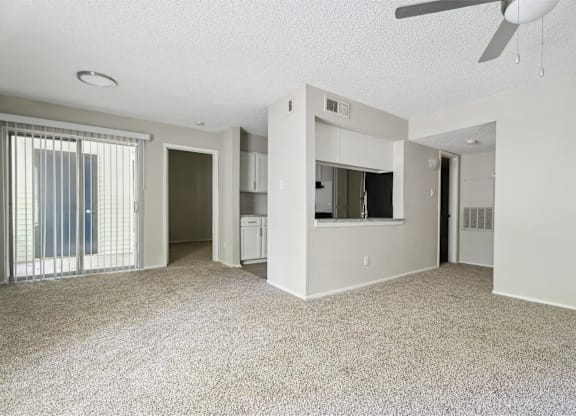 A spacious living room with a ceiling fan and carpeted floor.