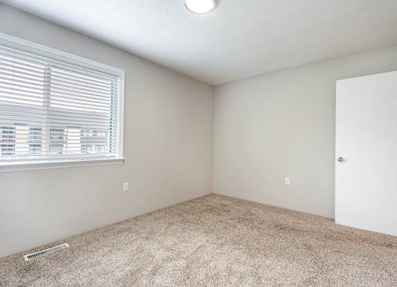 A room with a carpeted floor, a window with blinds, and a door.