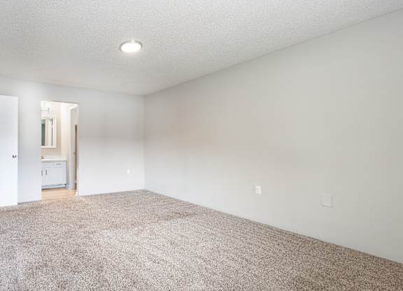 A large, empty room with a carpeted floor and a doorway leading to another room.