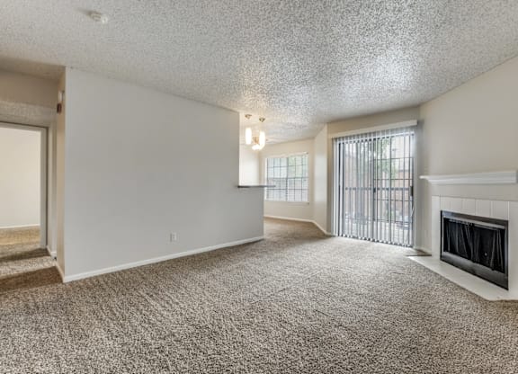 A sparsely furnished living room with a fireplace and a window with blinds.