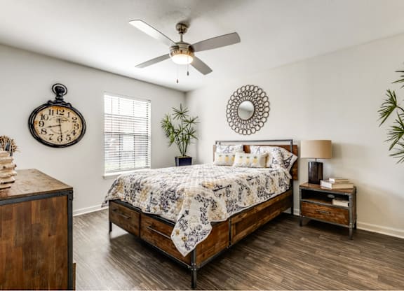 A bedroom with a bed, nightstand, and a plant.