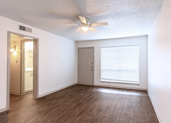 an empty living room with a ceiling fan and a window