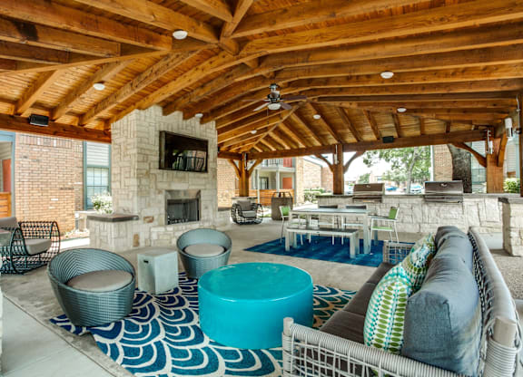 A large outdoor room with a stone fireplace and a blue and white rug.
