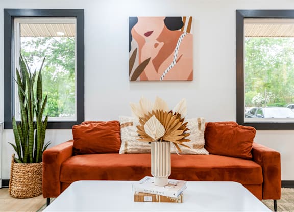 A living room with a red couch, a white coffee table, and a painting on the wall.