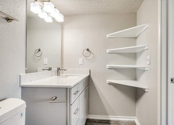 A bathroom with a white counter top and a mirror above it.