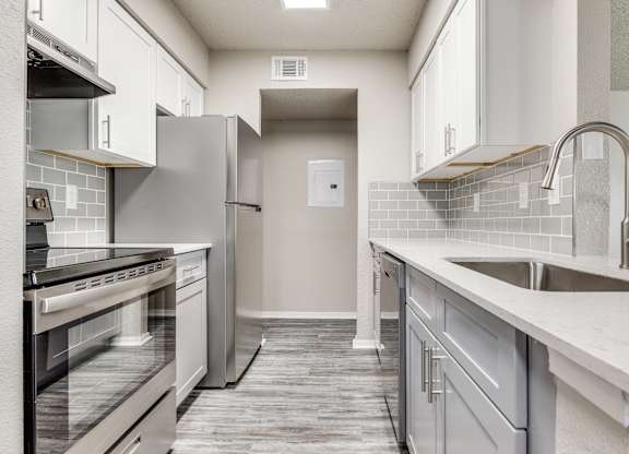 A kitchen with a white tile backsplash and a white sink.