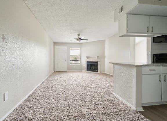 A sparsely furnished living room with a carpeted floor and a ceiling fan.