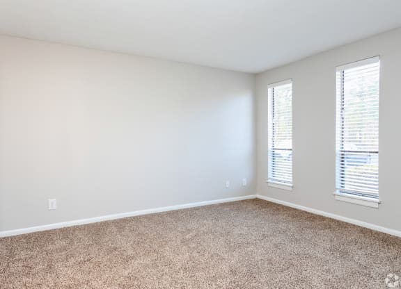 an empty room with carpet and two windows